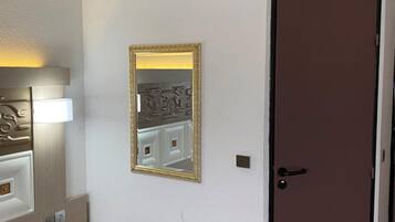 A hotel room with a bed, bedside table, lamp, mirror, and a door.