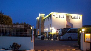 A hotel with a 'HOTEL GRILL' sign, a fenced entrance, and a bus parked outside. - Hotel Kimotel (Epone)