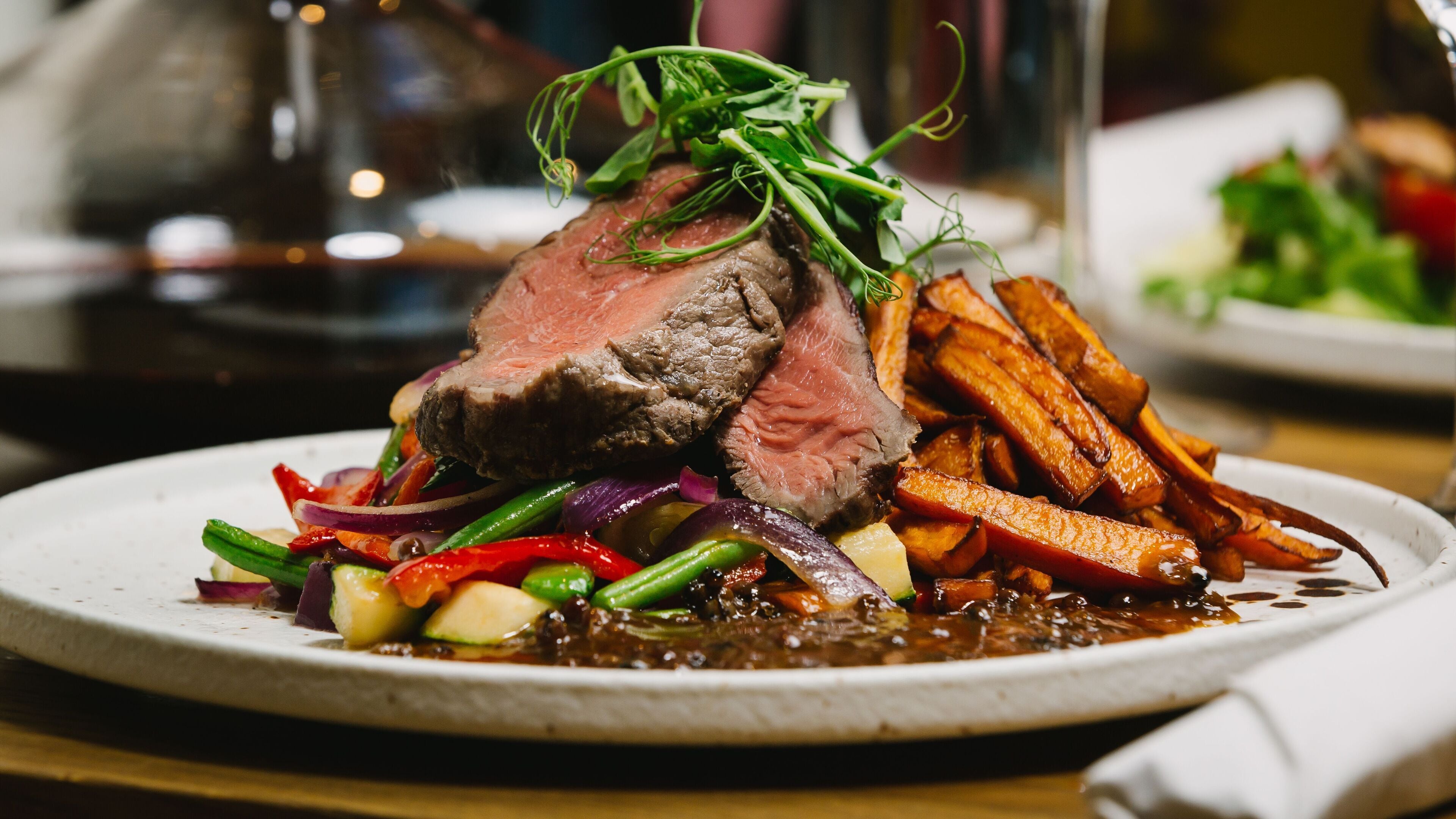 A plate of food with a slice of meat, vegetables, and a sauce.