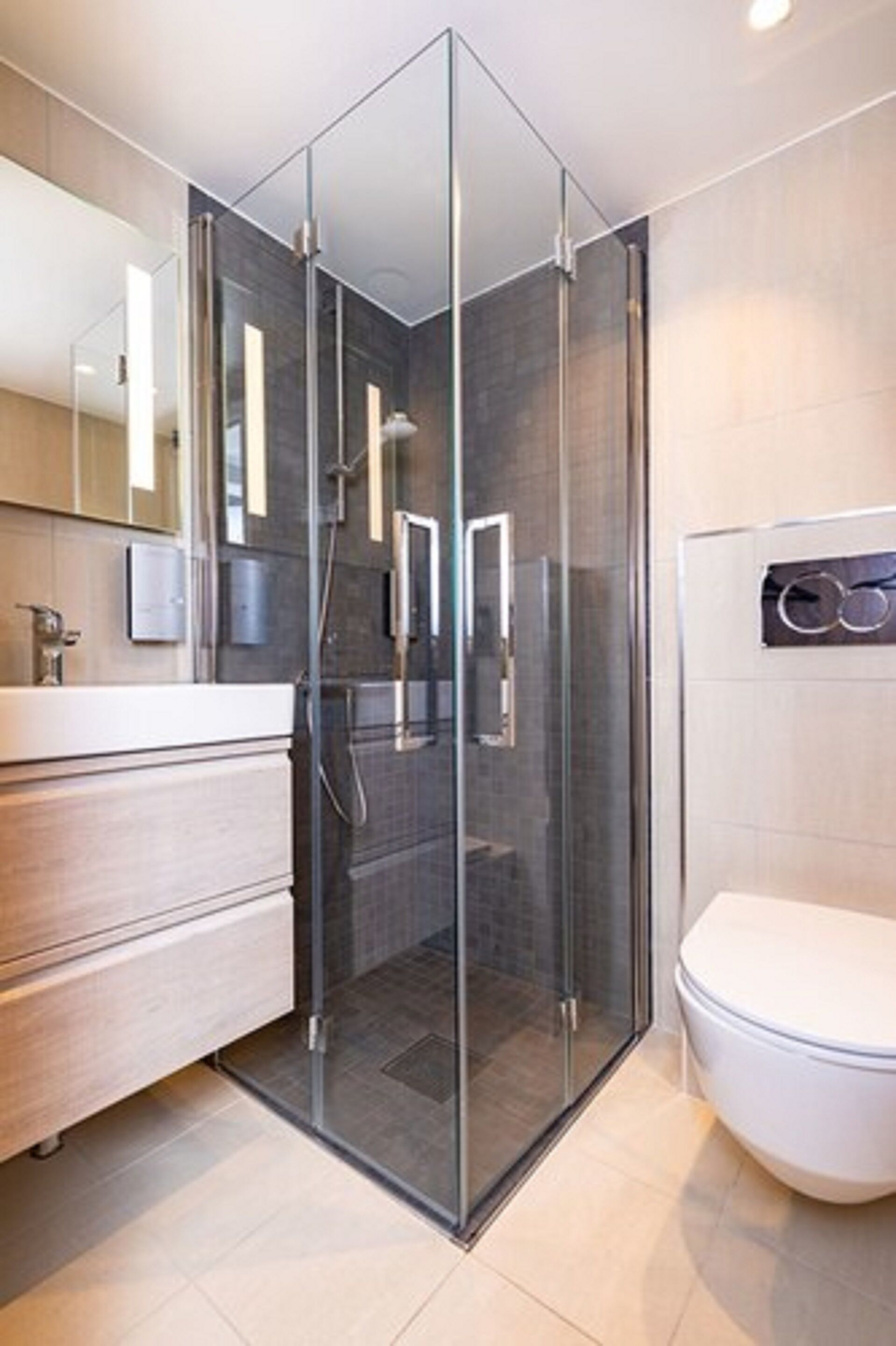Un baño moderno con ducha de vidrio, inodoro blanco y tocador de madera con espejo.
