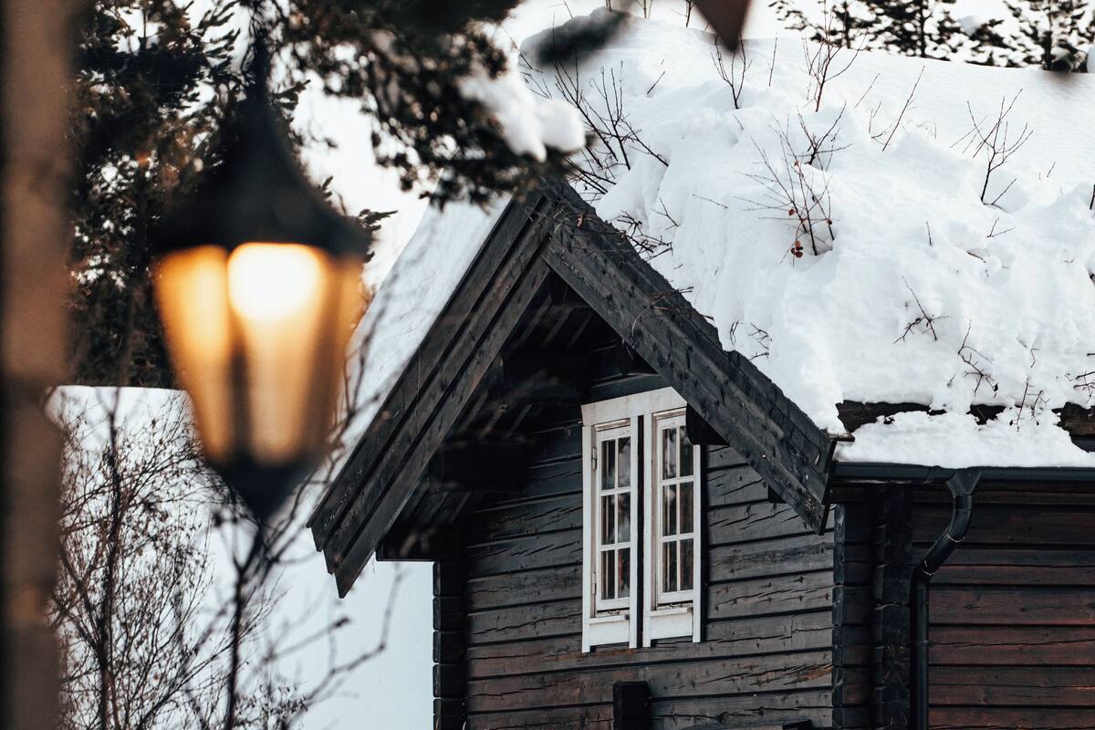 A wooden house with two windows and a garage door, surrounded by snow.