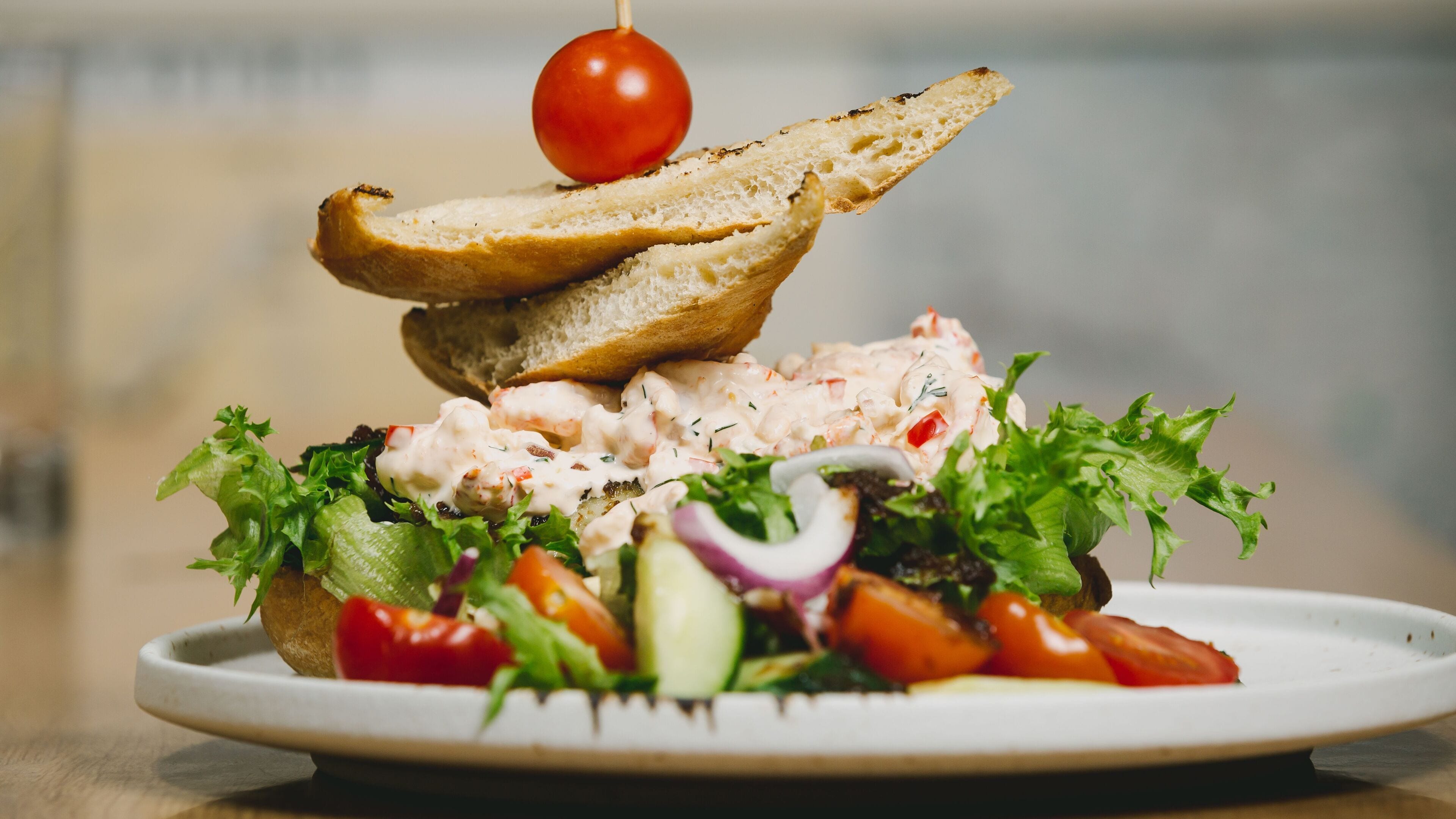 Un plato con ensalada, una rebanada de pan y un tomate cherry.