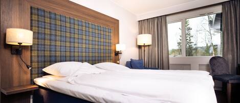 A hotel room with a large bed, two bedside lamps, a headboard with a plaid pattern, a chair, and a window with curtains.