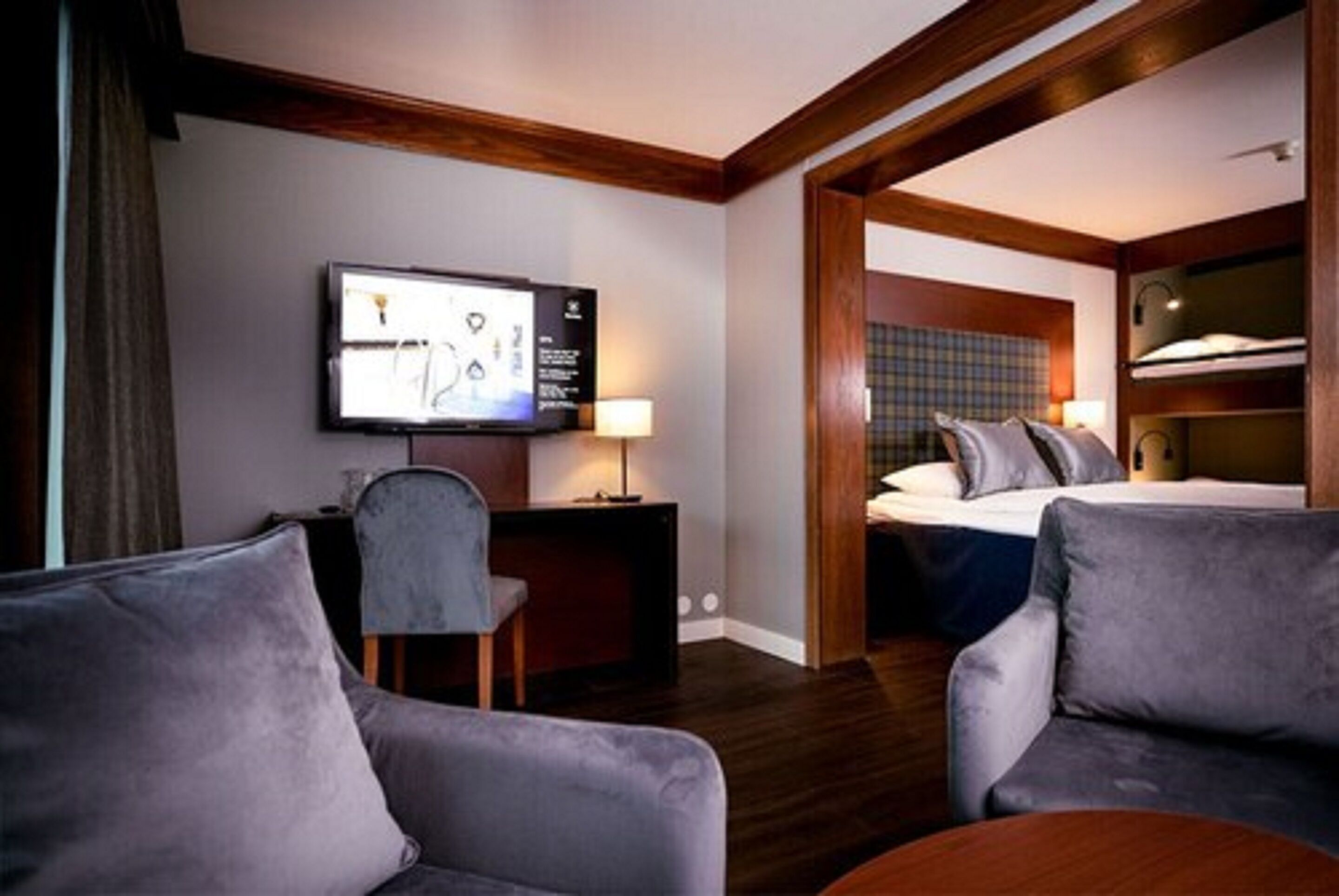 A hotel room with a TV, a desk, a chair, a bed, and a sofa.