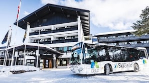 A bus with 'SkiGeilo' branding parked in front of a building with multiple floors and a ski lift visible in the background. - Bardøla Fjelltun (Hol)