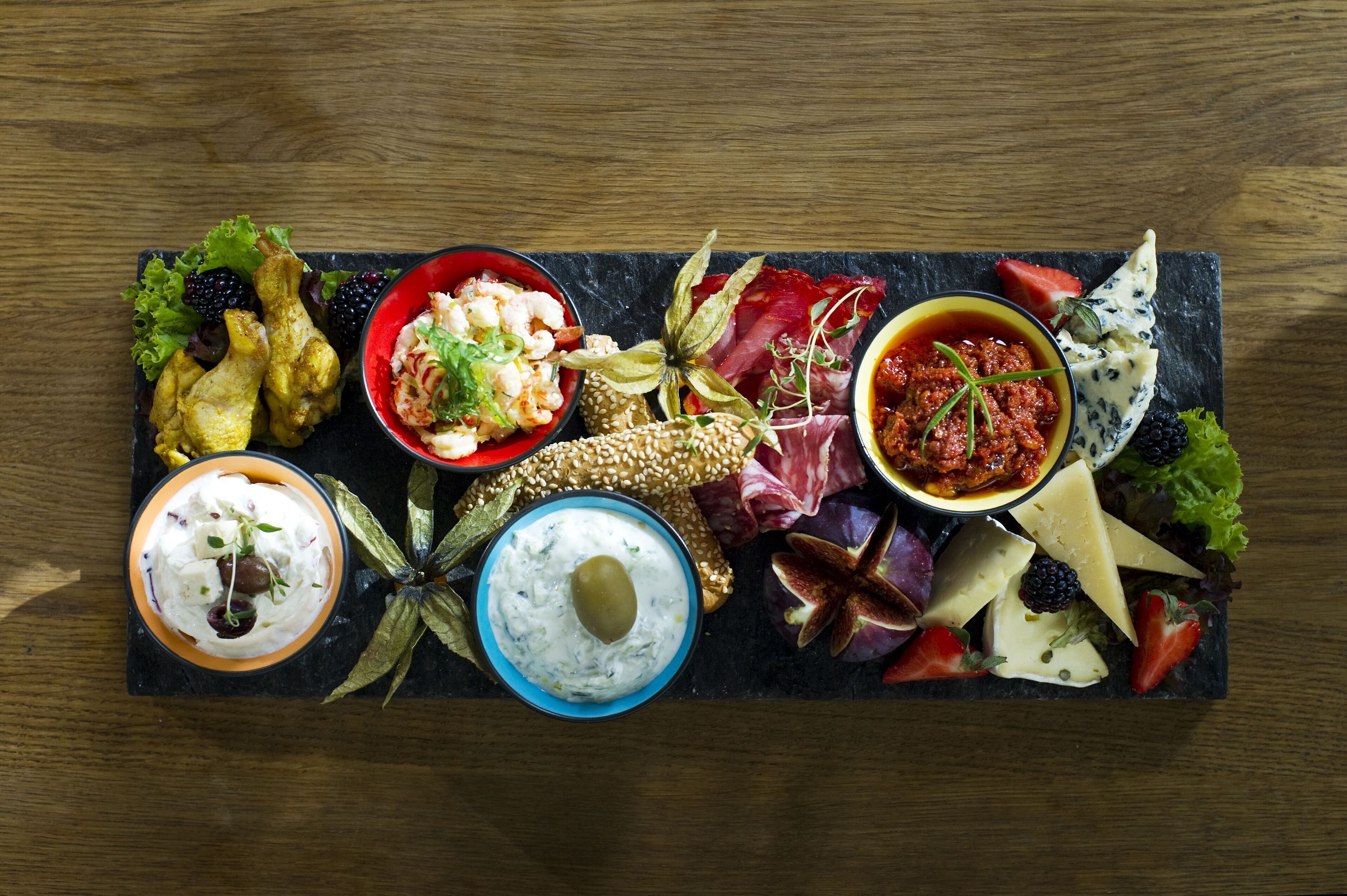 Un tagliere con diversi formaggi, salumi, frutta e salse.