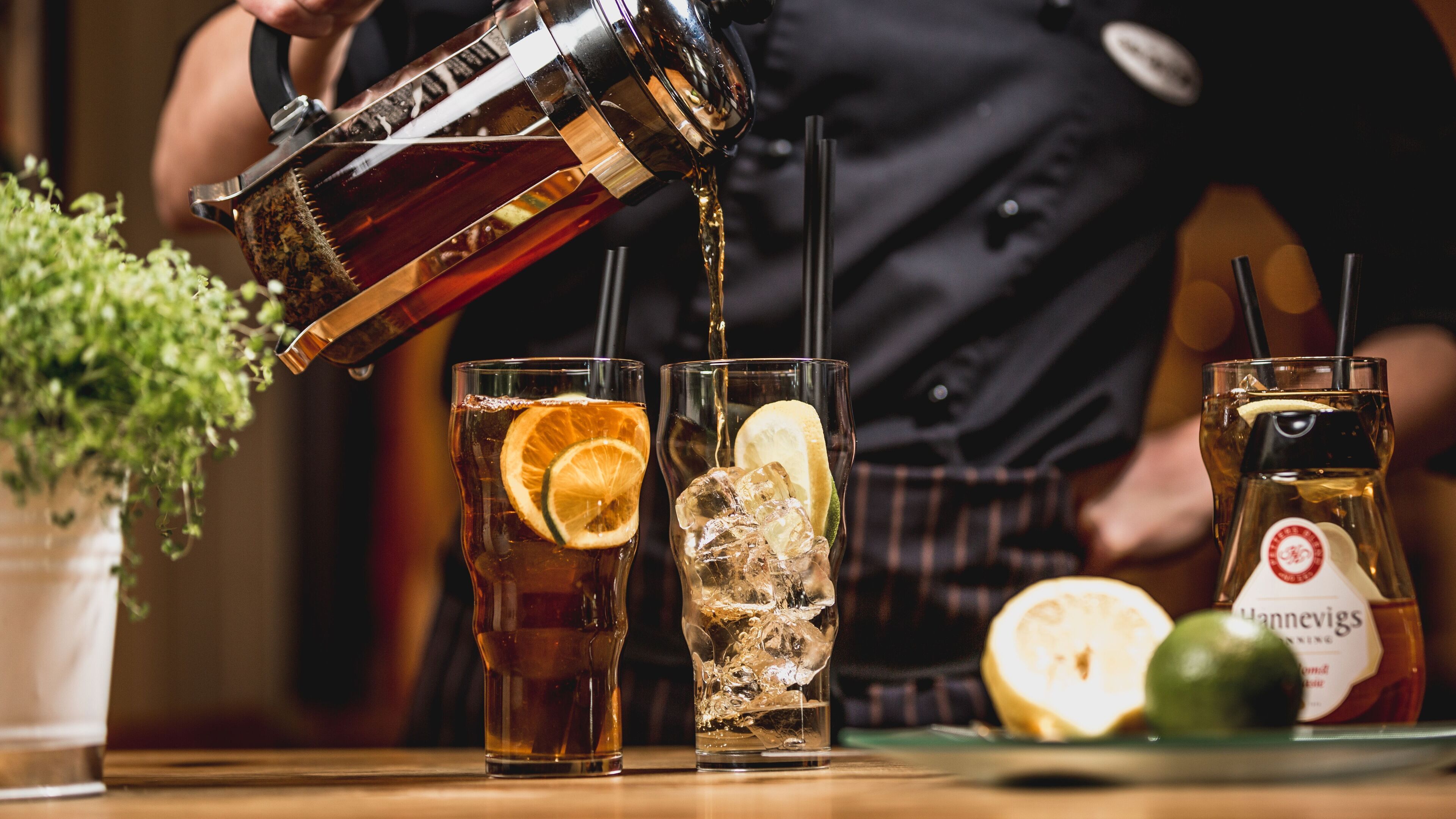 En bartender hælder en mørk væske i et glas med is og et appelsinstykke.