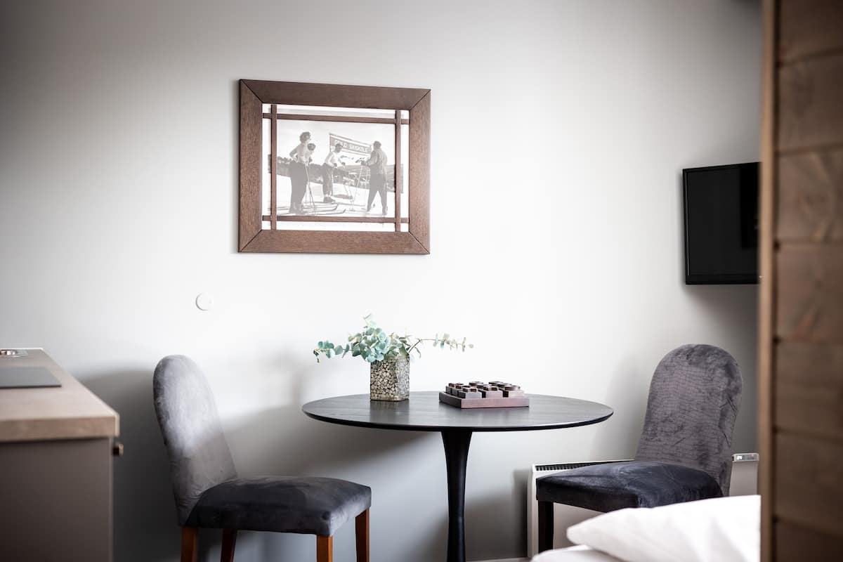 A hotel room with a round table, two chairs, a framed picture on the wall, a small plant, and a bed.
