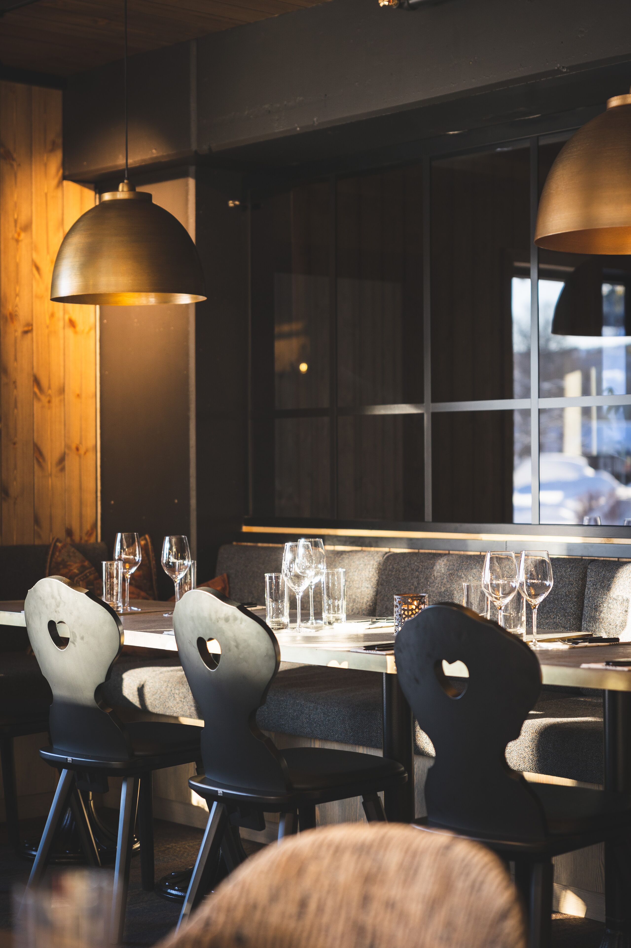 Een restaurantinterieur met een houten wand, grote hanglampen en uitzicht door een raam.