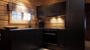 A modern kitchen with dark cabinetry, a window with plaid curtains, and a built-in oven. - Bardøla Fjelltun (Hol)
