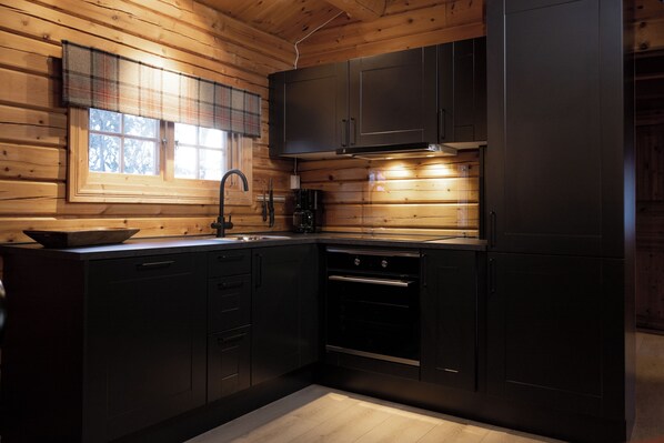 A modern kitchen with dark cabinetry, a window with plaid curtains, and a built-in oven.