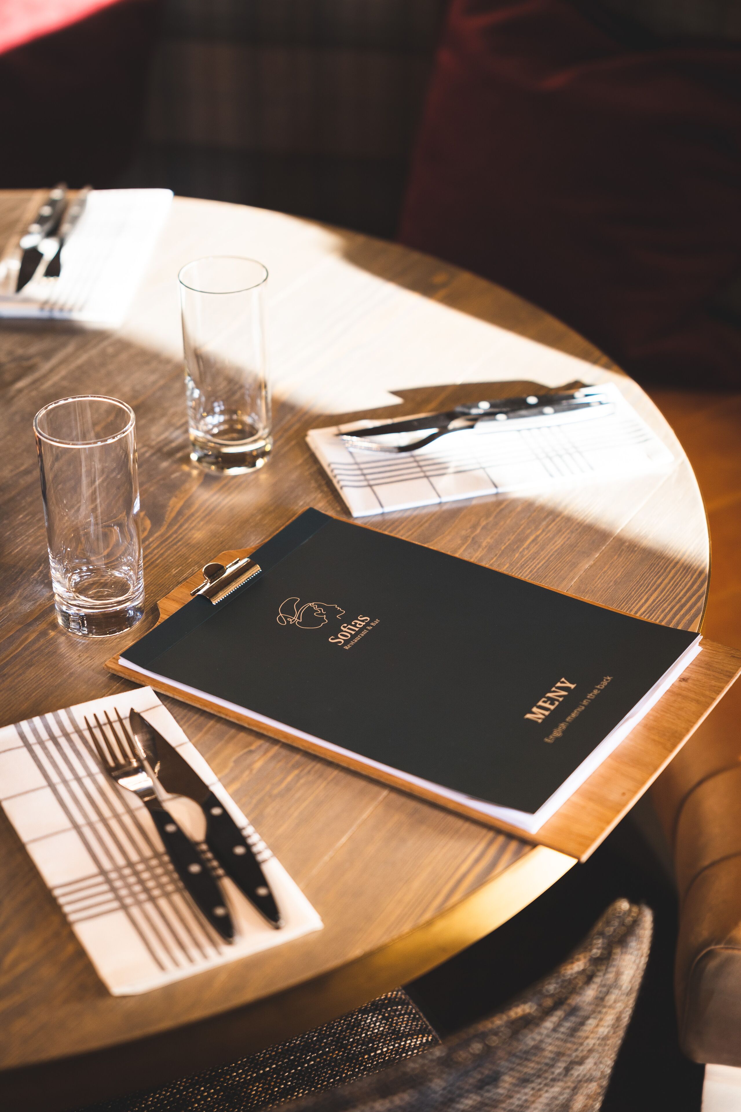 A neatly arranged dining table with a menu, glasses, and cutlery.