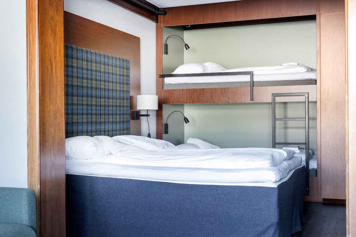A hotel room with a bunk bed, a desk, a lamp, and a plaid-patterned wall hanging.