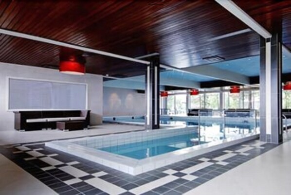 Un área de piscina interior moderna con suelo a cuadros, ventanas amplias y detalles en rojo.