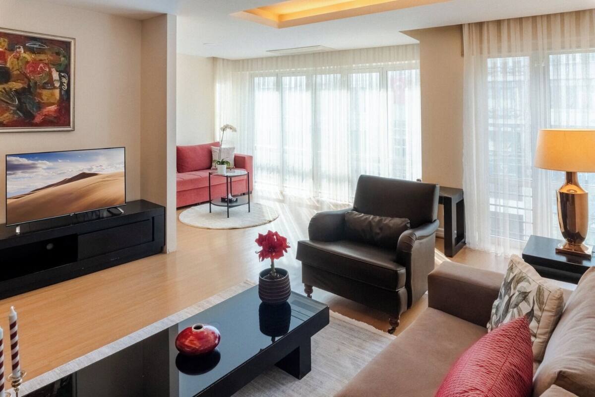 Una sala de estar moderna con una televisión de pantalla plana, un sofá, un sillón, una mesa de centro y una lámpara.