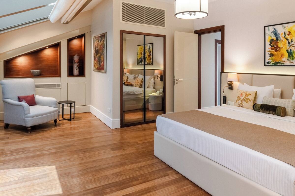 Un dormitorio moderno con una cama grande, una silla, una mesita y una puerta corredera que da al baño.