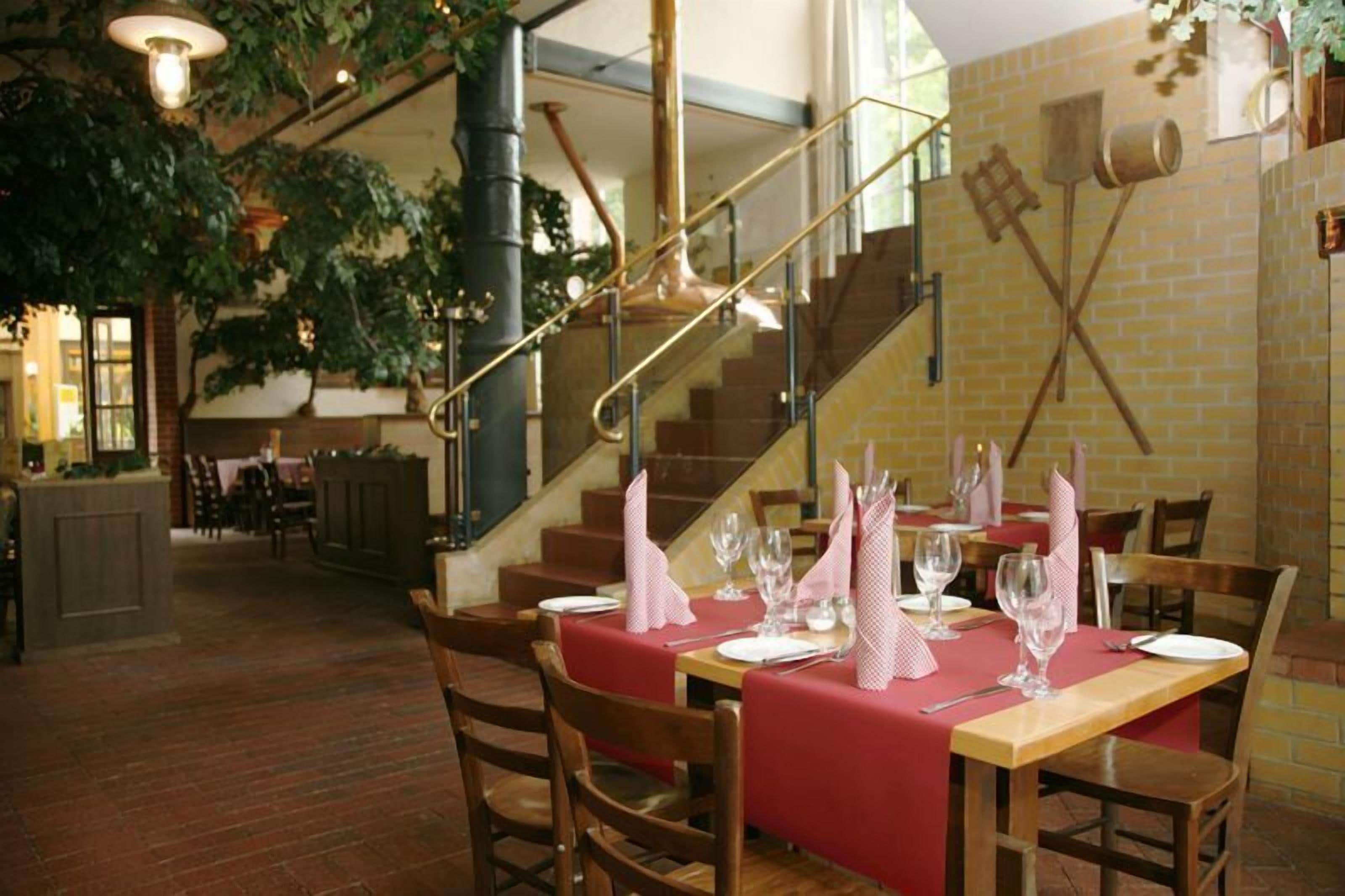 Un restaurant aux murs de briques, aux tables et aux chaises en bois. On y trouve un escalier avec une rampe et une plante suspendue au plafond.