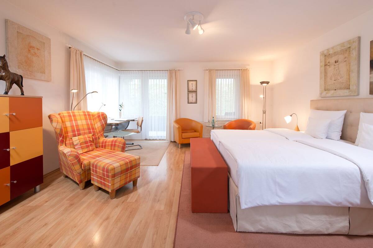 Una habitación de hotel con cama, sillón, escritorio y cómoda.
