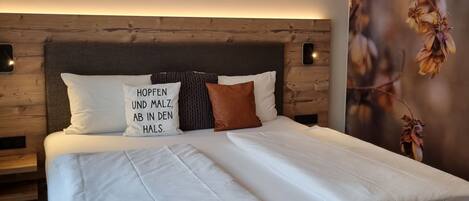 Un lit bien fait, avec du linge de lit blanc et un oreiller orné d’un motif, une tête de lit en bois et un mur décoré d’une fresque florale.