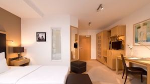 Habitación de hotel con cama, mesita de noche, lámpara, escritorio, silla, armario y un cuadro en la pared.