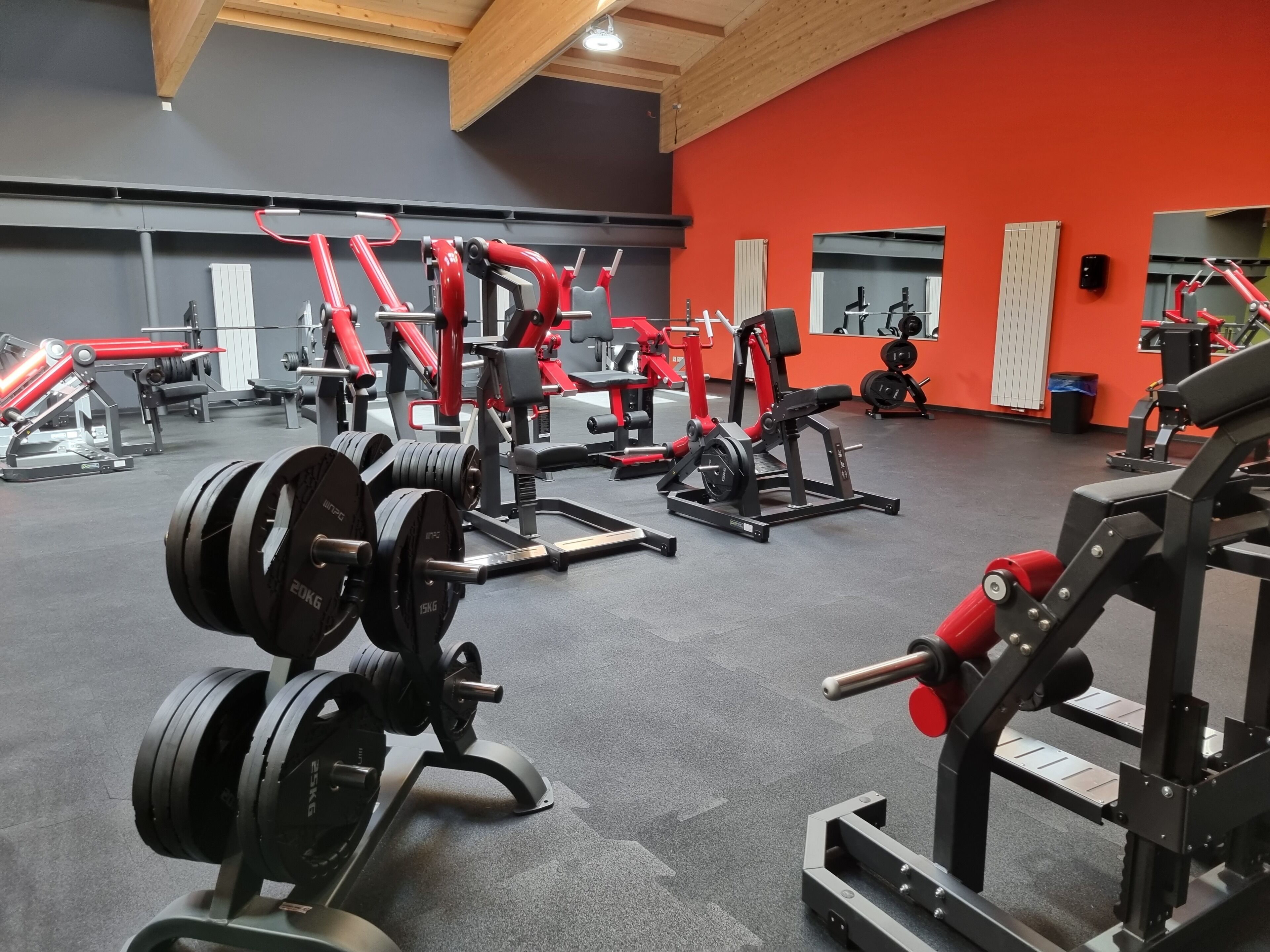 A gym with various weightlifting equipment, including barbells and weight plates, and a red wall.