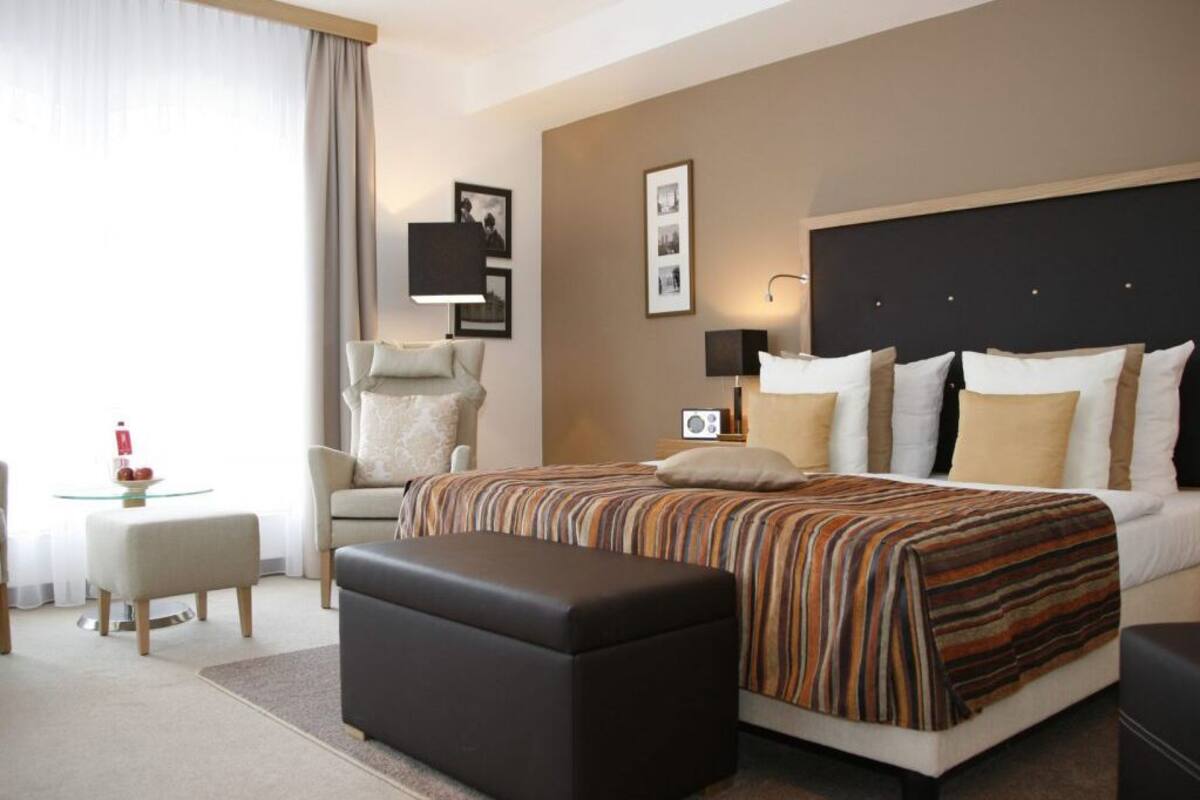 Una habitación de hotel con una cama grande, una silla, una mesita y una lámpara.