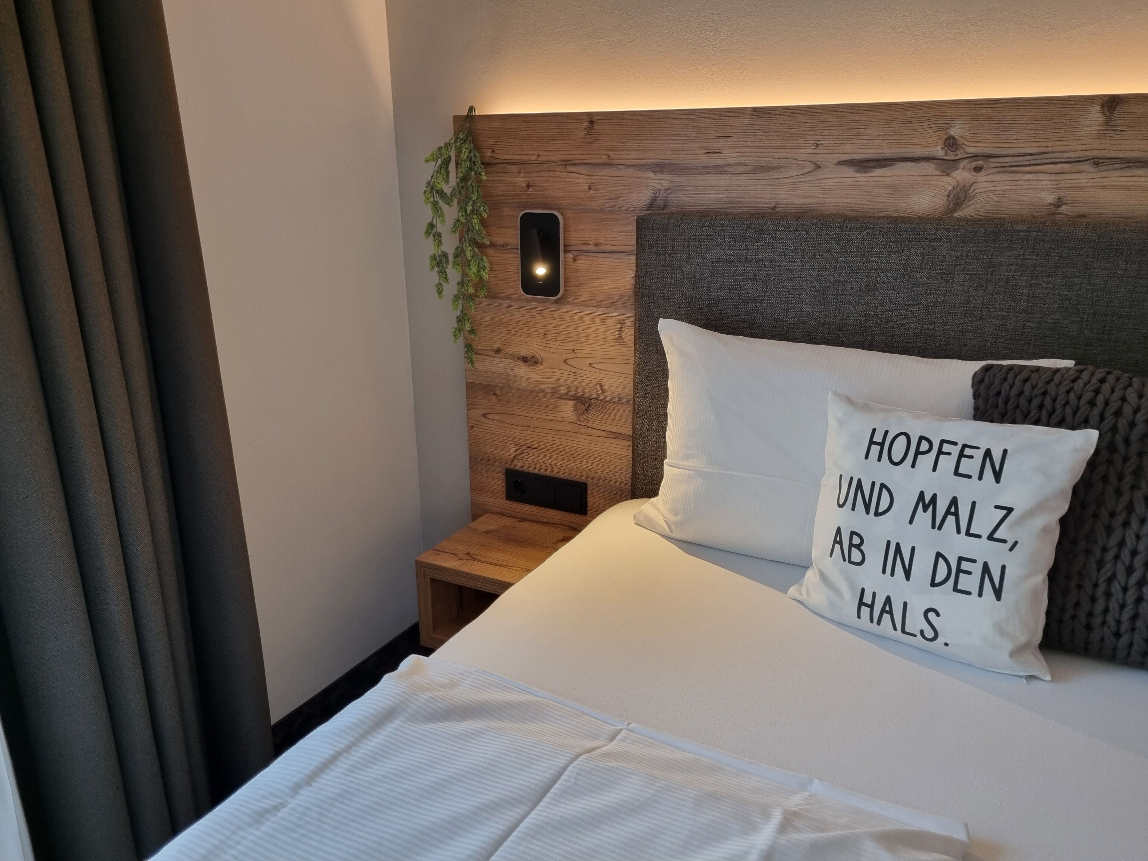 Una cama bien hecha con un cojín que dice "HOPFEN UND MALZ, AB IN DEN HALS".