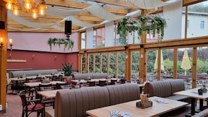 Un comedor interior con mesas y asientos tipo banca, ventanas amplias y plantas colgantes.
