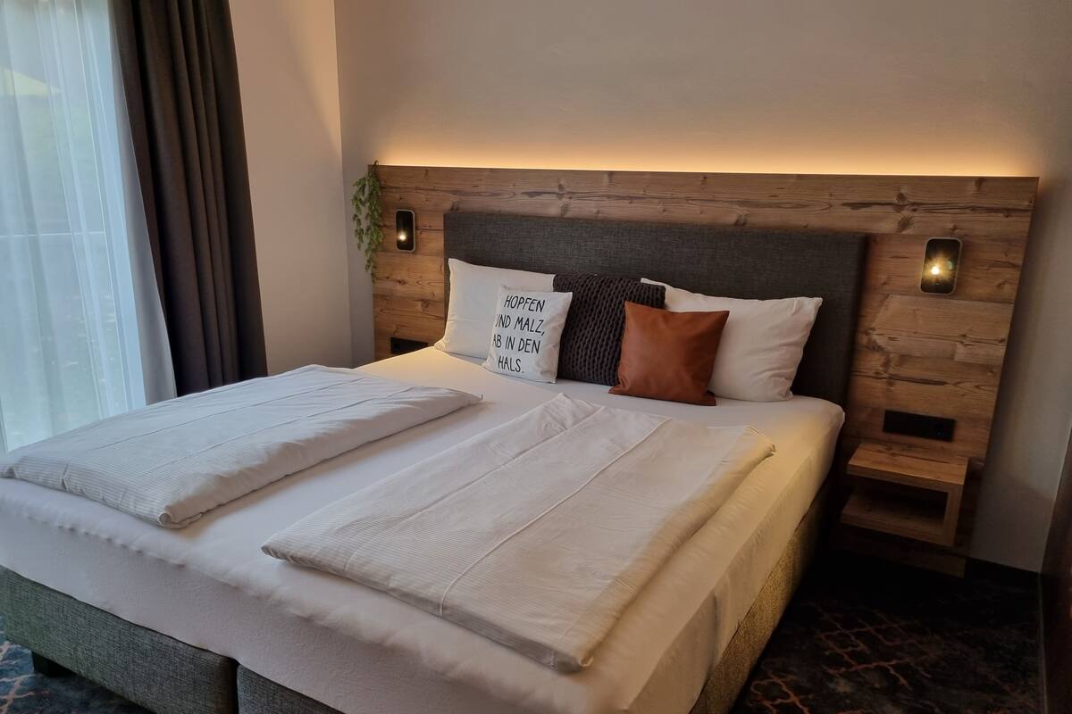 Una cama bien hecha con sábanas blancas y dos almohadas, cabecera de madera con iluminación integrada, y una alfombra estampada.