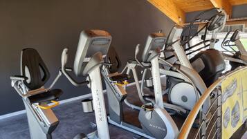 A gym with multiple cardio machines, including elliptical trainers and a stationary bike, under a wooden ceiling.