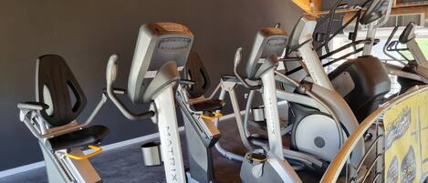 Un gimnasio con varias máquinas de cardio, incluyendo elípticas y una bicicleta estática, bajo un techo de madera.