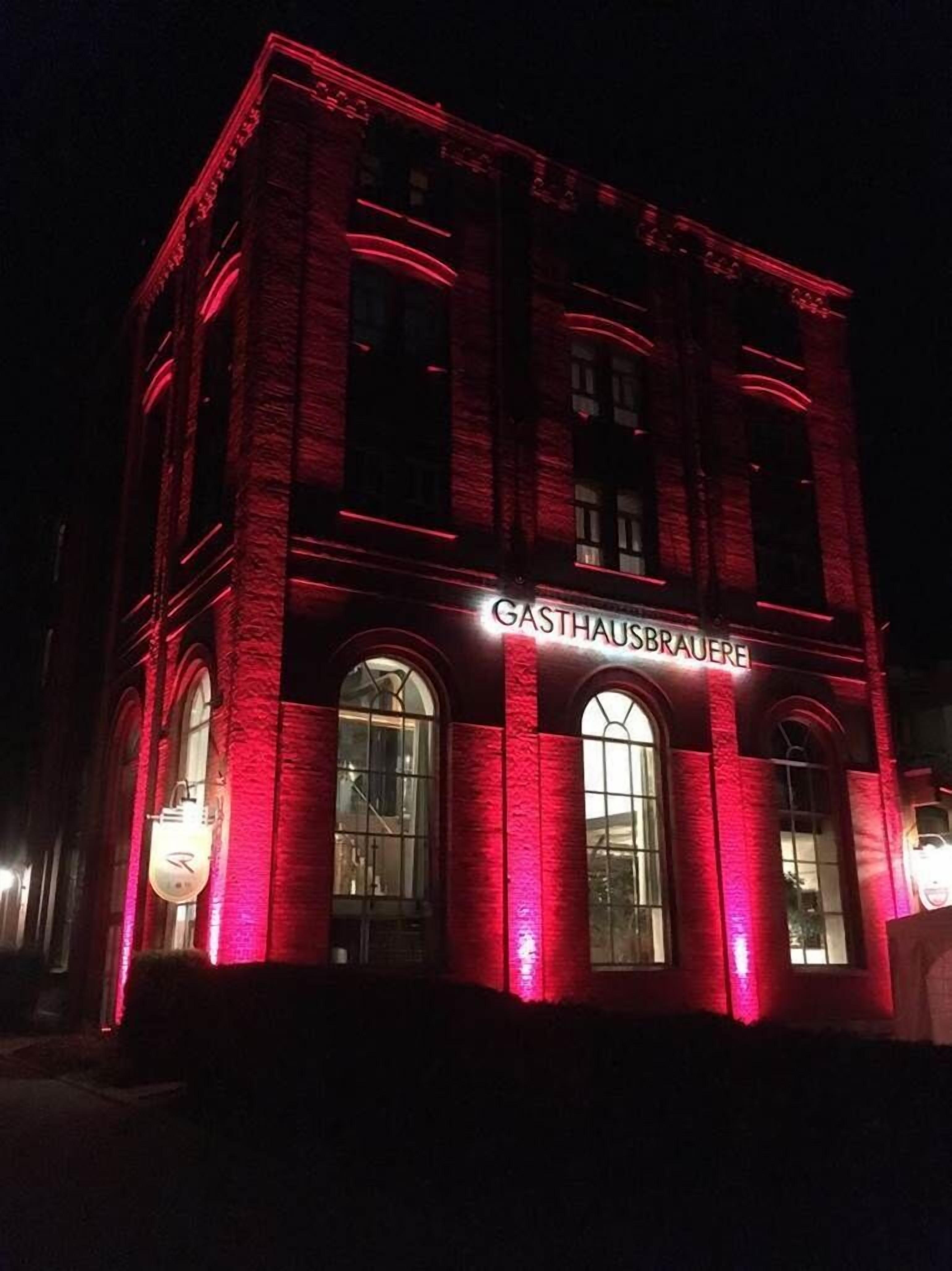 Un edificio con fachada iluminada en rojo y el nombre 'GASTHAUSBRAUERE' exhibido sobre la entrada.