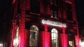 Un edificio con fachada iluminada en rojo y el nombre 'GASTHAUSBRAUERE' exhibido sobre la entrada.