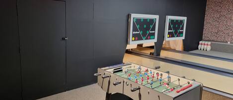 Una habitación con una mesa de futbolín, dos pistas de bolos y un letrero de neón que dice "Red Bull".
