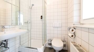 Un baño moderno con ducha de vidrio, lavamanos blanco y retrete.