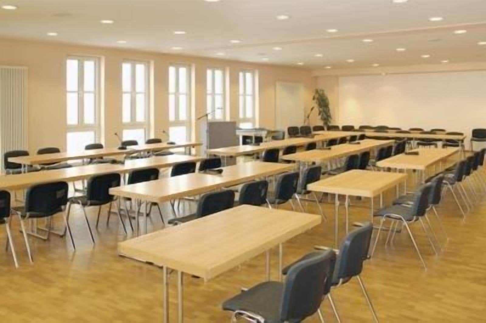 Une salle de conférence équipée de plusieurs tables et chaises, de grandes fenêtres et d’un écran de projection.
