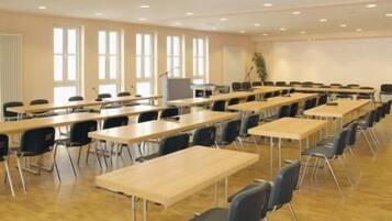 Une salle de conférence équipée de plusieurs tables et chaises, de grandes fenêtres et d’un écran de projection.