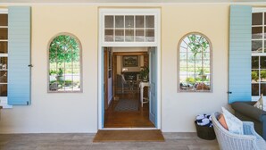 A covered porch with a wooden floor, a bench, and a wicker basket with folded towels. - Auberge Clermont (Franschhoek)
