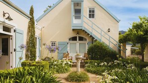 A two-story building with a light blue exterior, a central staircase, and a garden with various plants and flowers. - Auberge Clermont (Franschhoek)