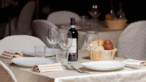 Mesa posta para refeição com pratos, copos, garrafa de vinho e cestas de pão.