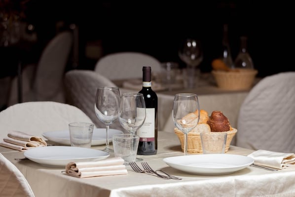 A table set for dining with plates, glasses, a wine bottle, and bread baskets. - Le Rotonde (Massarosa)