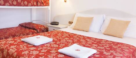 A hotel room with a bunk bed, a single bed, and a nightstand with a lamp.