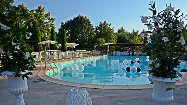 Uma área de piscina com uma piscina circular, elementos decorativos brancos e plantas em vasos.