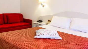Quarto de hotel com cama, sofá vermelho, mesa de cabeceira e luminária.