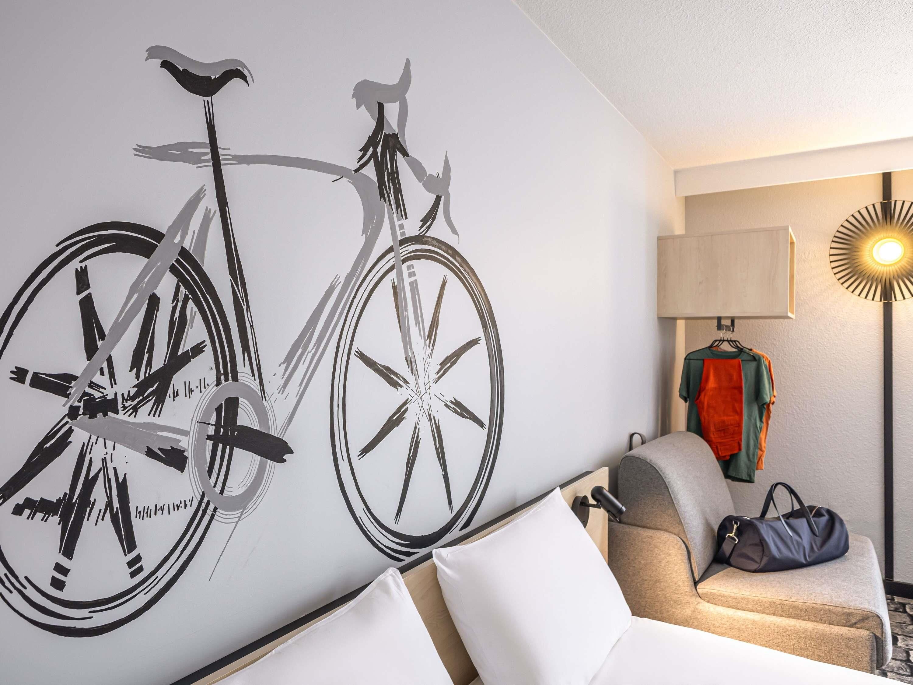Une pièce décorée avec une œuvre d’art représentant un vélo accroché au mur, un canapé, une lampe et un vêtement suspendu.