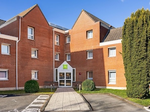 A red-brick building with a central entrance, multiple windows, and a green sign. - Ibis Styles Lille Villeneuve d’Ascq (Villeneuve-d'Ascq)