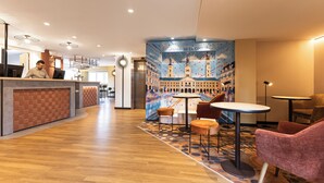 Un hall d’hôtel comprenant un comptoir d’accueil, un espace salon et une fresque représentant un paysage urbain.