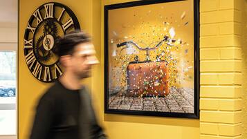 A wall with a large clock and a framed picture of a suitcase with confetti.