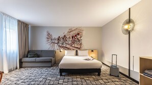 Une chambre d’hôtel avec un lit, un canapé, une valise, une lampe et une œuvre d’art murale.