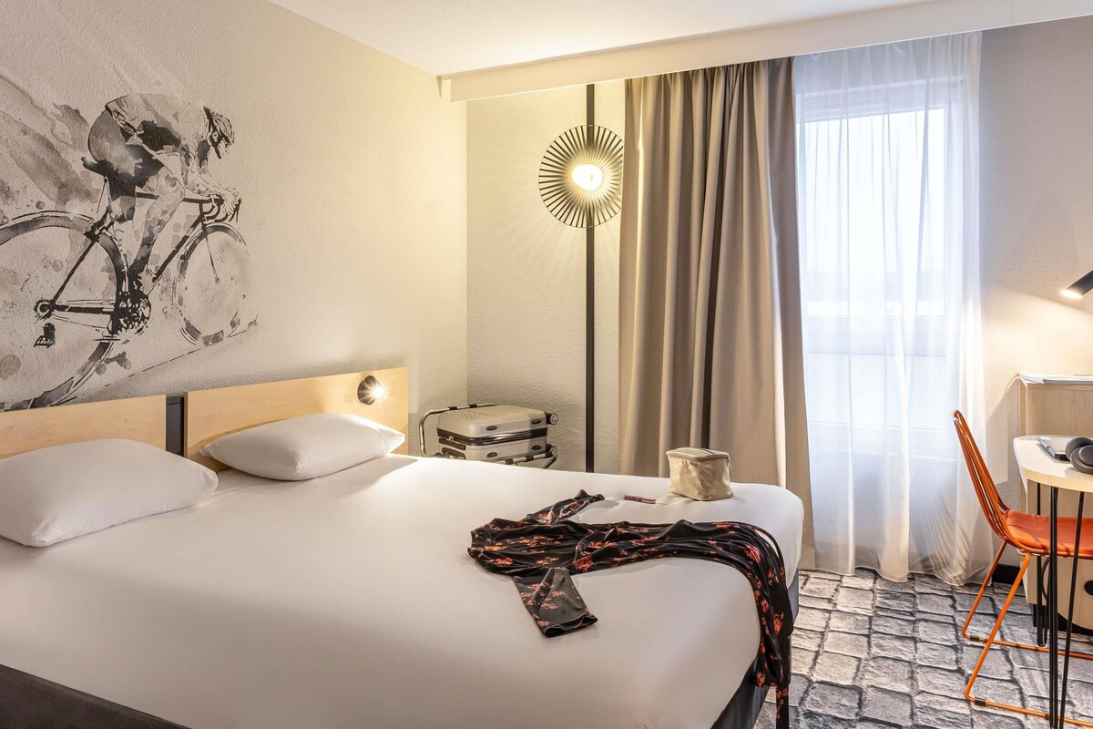 Habitación de hotel con cama, escritorio, silla, lámpara y un cuadro en la pared.